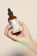Load image into Gallery viewer, A hand holding a 4 oz bottle of CRUDE Cleanse
